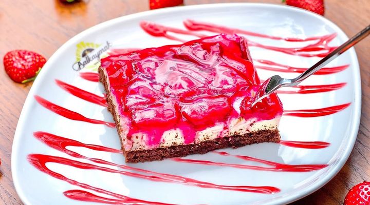 A strawberry cake slice on a Balkaymak plate, fresh strawberries around it