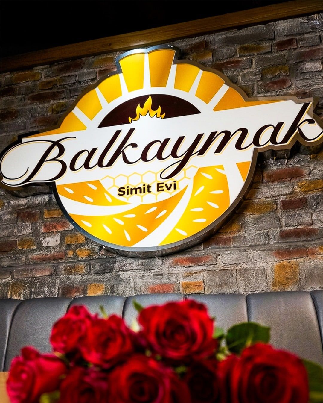 Das beleuchtete Balkaymak-Logo an der Backsteinwand, rote Rosen davor